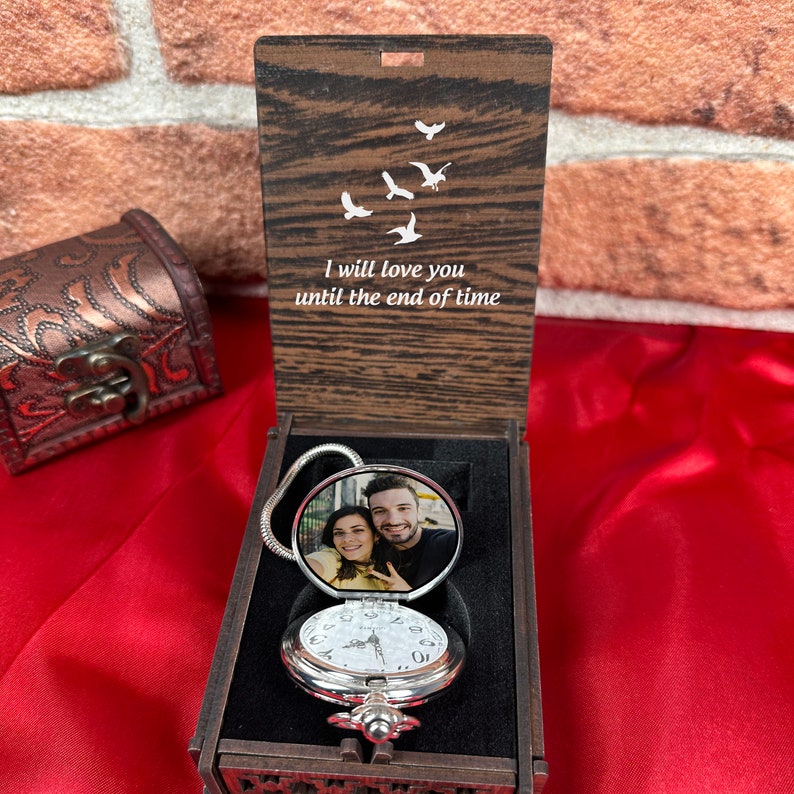 May include: A wooden box with a hinged lid, containing a silver pocket watch with a photo of a couple on the front. The lid of the box is engraved with the words "I will love you until the end of time" and a design of flying birds.