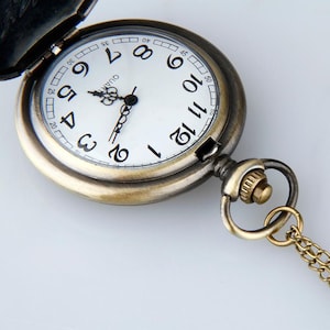 May include: A vintage-style pocket watch with a white face and black Roman numeral hour markers. The watch has a gold-toned metal case and a chain.