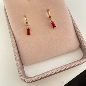 May include: A pair of gold hoop earrings with a dangling red rectangular stone.