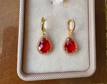 May include: A pair of gold earrings with red teardrop-shaped stones set in a delicate gold filigree design. The earrings are displayed in a white velvet box.