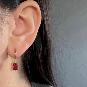 以下が含まれることがあります： 赤い正方形の宝石がぶら下がった、金のフープイヤリング