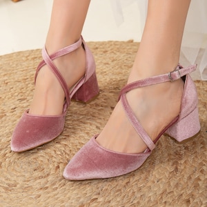 Puede incluir: Un par de zapatos de tacón de terciopelo rosa polvoriento con correas cruzadas y cierre de hebilla.