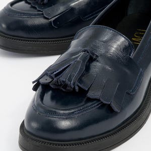 Può includere: Un paio di mocassini in pelle blu navy con dettagli a nappe. Le scarpe hanno la punta arrotondata e una suola spessa nera. Uno stile classico.