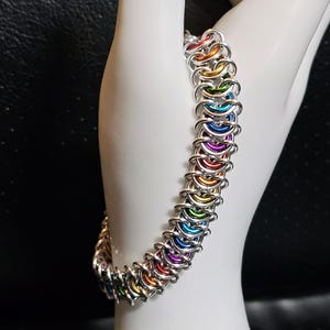 May include: A rainbow colored chainmail bracelet made of silver metal rings.