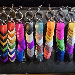 May include: A collection of keychains with colorful, scale-like pendants. Each keychain features a silver ring and clasp, with pendants in various colors including red, orange, pink, green, and blue. The pendants are arranged in a layered pattern.