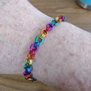 May include: A rainbow colored chain bracelet made of metal. The bracelet is on a person's wrist.