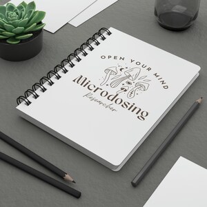 Peut inclure: Un carnet à spirales blanc avec le texte "Open your mind" et "Microdosing researcher" avec un graphique de champignon.