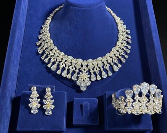 May include: A luxurious jewelry set displayed on a blue velvet surface. The set includes a sparkling necklace, earrings, and a bracelet, all adorned with clear, brilliant-cut stones. The necklace is draped on a mannequin head.