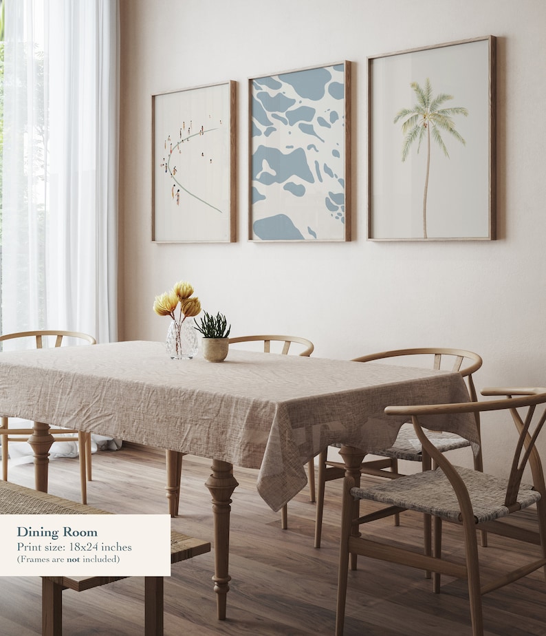 May include: A dining room with a light brown wooden table and six chairs. The table is set with a beige tablecloth and a vase of yellow flowers. Three framed prints hang on the wall behind the table. The prints feature a beach scene, a blue abstract design, and a palm tree. The text "Dining Room" and "Print size: 18x24 inches (Frames are not included)" is visible at the bottom of the image.