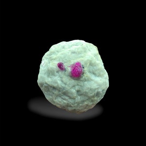 May include: A close-up of a rough, white rock with two bright red ruby crystals embedded in it.