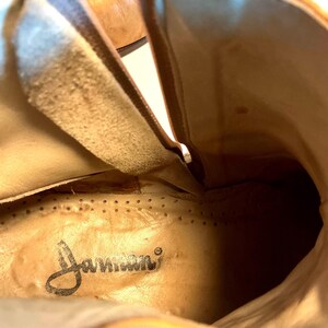 May include: Close-up interior view of a light brown leather boot. The boot's interior features a tan insole with the brand name "Janseen" printed in black script. The leather has a worn appearance.