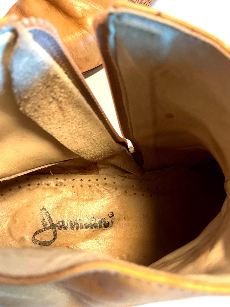 May include: Close-up interior view of a light brown leather boot. The boot's interior features a tan insole with the brand name "Janseen" printed in black script. The leather has a worn appearance.