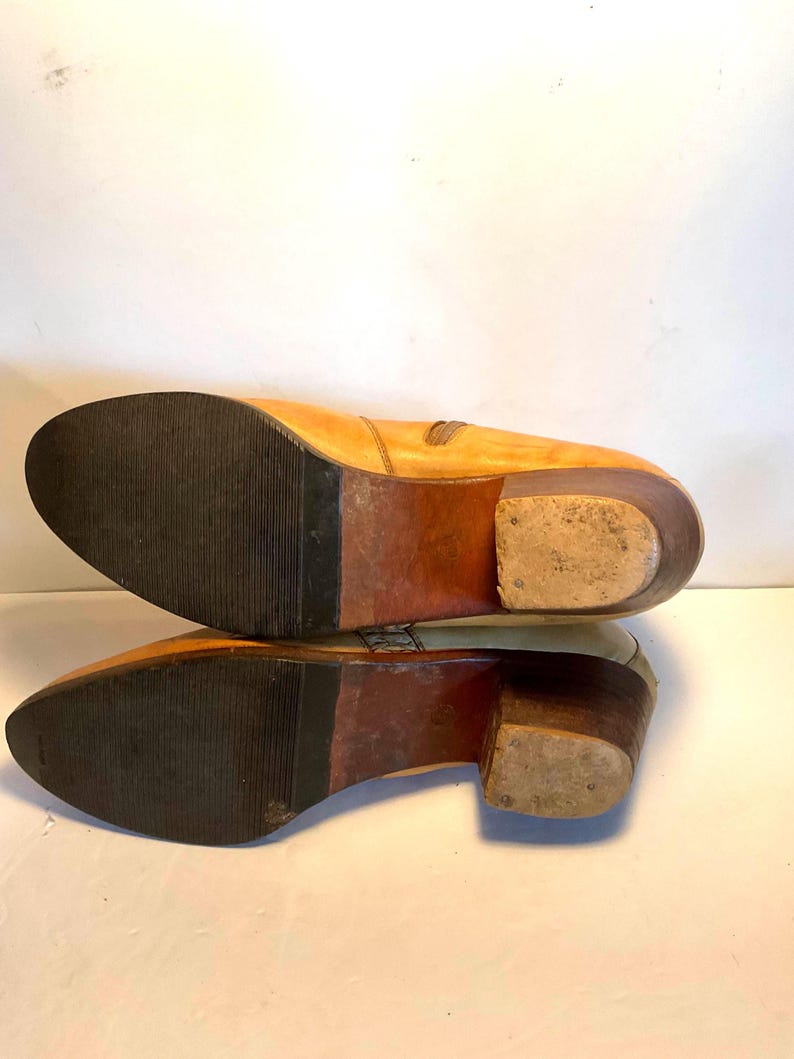 May include: A pair of light tan leather boots with a stacked heel. The soles are dark brown rubber with a textured pattern. The boots have a side zipper and a pointed toe. The heels are approximately 2 inches high.