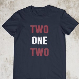 Puede incluir: Camiseta azul marino con las palabras "TWO ONE TWO" impresas en rojo en la parte delantera.