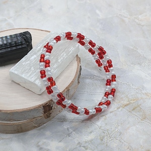 May include: A multi-strand wrap bracelet constructed from alternating red and white glass seed beads. The circular jewelry piece features a flexible wire design that coils around the wrist, showcasing a repeating pattern of vibrant red and opaque white beads.