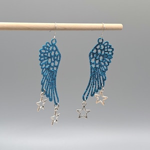 May include: A pair of drop earrings featuring blue glitter-covered wing-shaped cutouts. Each wing is suspended from a silver-toned hook and accented with two small, open-frame silver-toned star charms hanging from the bottom edge of the wings.