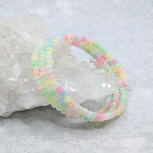 May include: A pastel-colored beaded wrap bracelet. The bracelet features small, round beads in shades of pink, yellow, green, and blue. The bracelet is wrapped multiple times and has a silver-colored clasp.