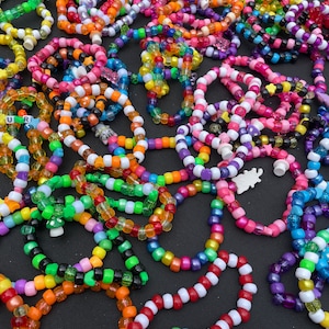 May include: A collection of colourful beaded bracelets with various patterns and designs, including some with letters spelling out words like "UR" and "UNITY".