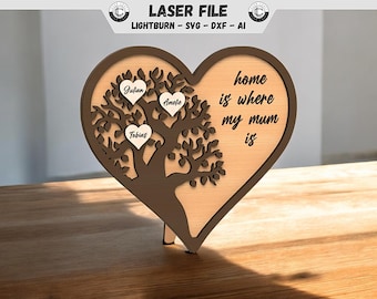 Puede incluir: Una placa de madera de color marrón en forma de corazón con un diseño de árbol y el texto "home is where my mum is". Tres corazones con los nombres "Julian", "Amelie" y "Tobias" están en las ramas del árbol.