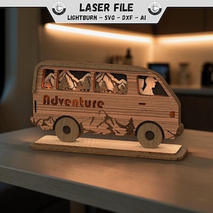 Puede incluir: Una pieza decorativa de madera cortada con láser que representa una furgoneta camper con una escena de montaña y bosque en capas en las ventanas. La palabra Adventure está cortada en el panel lateral. La furgoneta se asienta sobre una base.