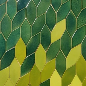 Op de afbeelding: Een muur bedekt met groene en gele ruitvormige tegels. De tegels zijn gerangschikt in een herhalend patroon, waardoor een geometrisch ontwerp ontstaat.