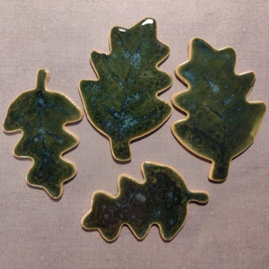 Op de afbeelding: Vier groene keramische eikenbladeren met een gespikkeld glazuur. De bladeren zijn van verschillende grootte en vorm.