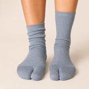 May include: A pair of mid-calf length, slate blue socks featuring a split-toe design. The socks are constructed from a ribbed knit fabric that extends from the ankle down to the toes, providing a textured appearance and a snug fit around the feet.