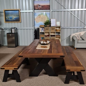May include: A large wooden table with a black X-shaped base and two matching benches. The table has a natural wood finish and is surrounded by a light brown floor.
