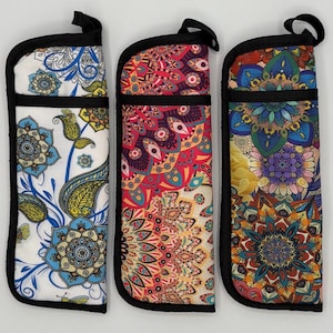 May include: Three decorative eyeglass cases with black trim and a loop at the top. The cases feature colorful floral and mandala patterns in shades of blue, red, yellow, and purple. The cases are designed to protect eyeglasses.