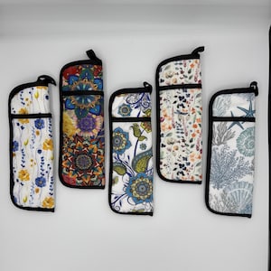 May include: Five vertical fabric cases with black trim, each featuring a distinct pattern: yellow and blue flowers, colorful mandalas, blue paisley and floral motifs, small multicolored wildflowers, and a blue and white sea life print.