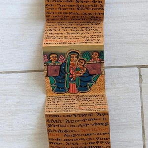 Pode incluir: Ícone ortodoxo etíope de madeira pintado à mão. A obra de arte retrata figuras e cenas religiosas, incluindo um santo a cavalo, a Virgem Maria com o Menino Jesus e outros santos. O ícone apresenta ilustrações e escrita detalhadas.