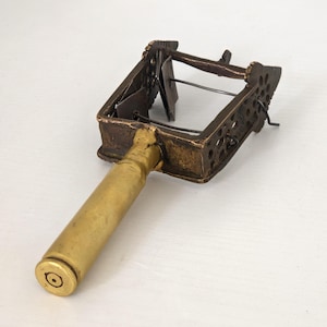 May include: An antique brass and metal tool with a rectangular cage-like structure and a cylindrical handle. The cage has decorative cutouts and a hinged mechanism. The handle is a brass cylinder. The tool has a vintage, aged appearance.