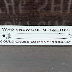 May include: White sticker with black text and a simple line drawing of a submarine. The text reads "Who knew one metal tube could cause so many problems."