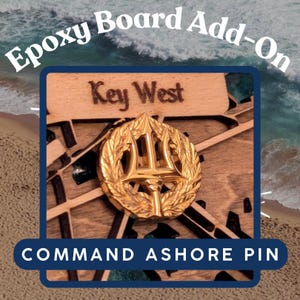 May include: A gold-coloured metal pin with a trident and laurel wreath design. The pin says "Key West" and "Command Ashore Pin".