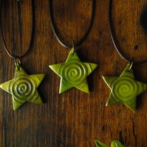 Puede incluir: Tres colgantes en forma de estrella verde con un patr&oacute;n de espiral cuelgan de cordones marrones sobre un fondo de madera.