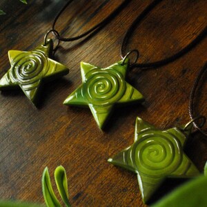 Puede incluir: Tres colgantes de estrella verde con un dise&ntilde;o en espiral, colgando de cordones marrones.