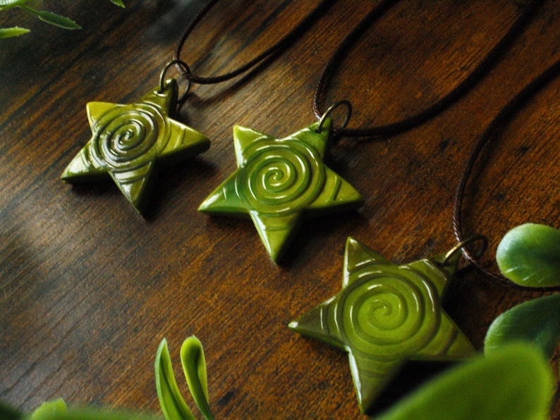 Puede incluir: Tres colgantes de estrella verde con un dise&ntilde;o en espiral, colgando de cordones marrones.