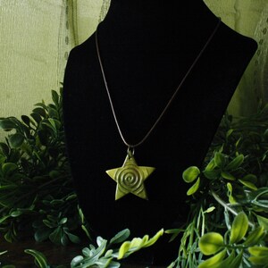 Puede incluir: Un collar con un colgante de estrella dorada con un dise&ntilde;o en espiral en la estrella. El collar est&aacute; en un expositor de terciopelo negro.