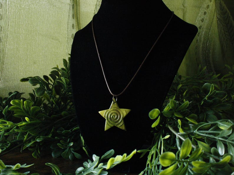 Puede incluir: Un collar con un colgante de estrella dorada con un dise&ntilde;o en espiral en la estrella. El collar est&aacute; en un expositor de terciopelo negro.
