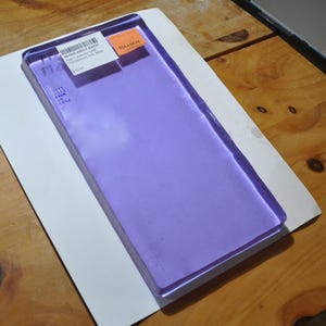 Może przedstawiać: Prostokątny, przezroczysty arkusz lawendy z etykietą z napisem "Note Lavender Sheet Transparent Tex, Bullseye". Arkusz leży na białej kartce papieru, spoczywając na drewnianej powierzchni.