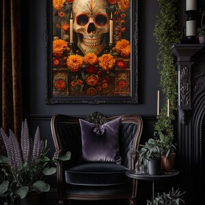 K&ouml;nnte beinhalten: Ein gerahmtes Kunstwerk zeigt einen Totenkopf, verziert mit orangefarbenen und roten Blumen, Kerzen und dekorativen Elementen. Der Totenkopf ist der Mittelpunkt, vor einem dunklen Hintergrund. Das Kunstwerk h&auml;ngt &uuml;ber einem Samtsessel mit einem lila Kissen.
