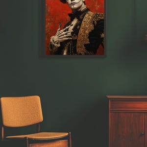 May include: Framed artwork depicting a person in Day of the Dead attire. The person wears a black and gold jacket, a floral hat, and skull makeup. The background is red with floral patterns. A wooden chair and cabinet are in the foreground.
