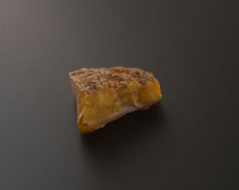 May include: A piece of amber, a fossilized tree resin, with a yellow and brown color. The amber is irregularly shaped and has a smooth surface.