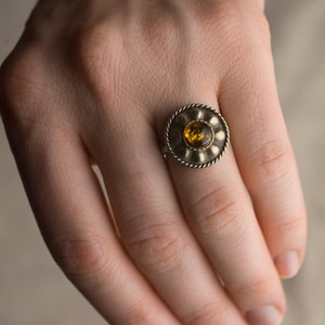 Könnte beinhalten: Ein silberner Ring mit einem runden Bernstein, der in einer dekorativen Fassung sitzt.