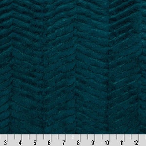 May include: Teal-colored fabric with a chevron pattern. The fabric has a soft, textured appearance, with the pattern running diagonally across the surface. A ruler is at the bottom, showing measurements in inches.