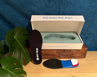 Puede incluir: Un par de plantillas para zapatos negras con detalles azules y rojos. Las plantillas están en una caja blanca con el texto "STEP RIGHT, FEEL RIGHT" y "www.orion-foot.com".