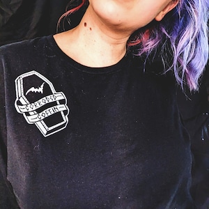 May include: Black t-shirt with a white graphic of a coffin with a bat and the text "Corroded Coffin".