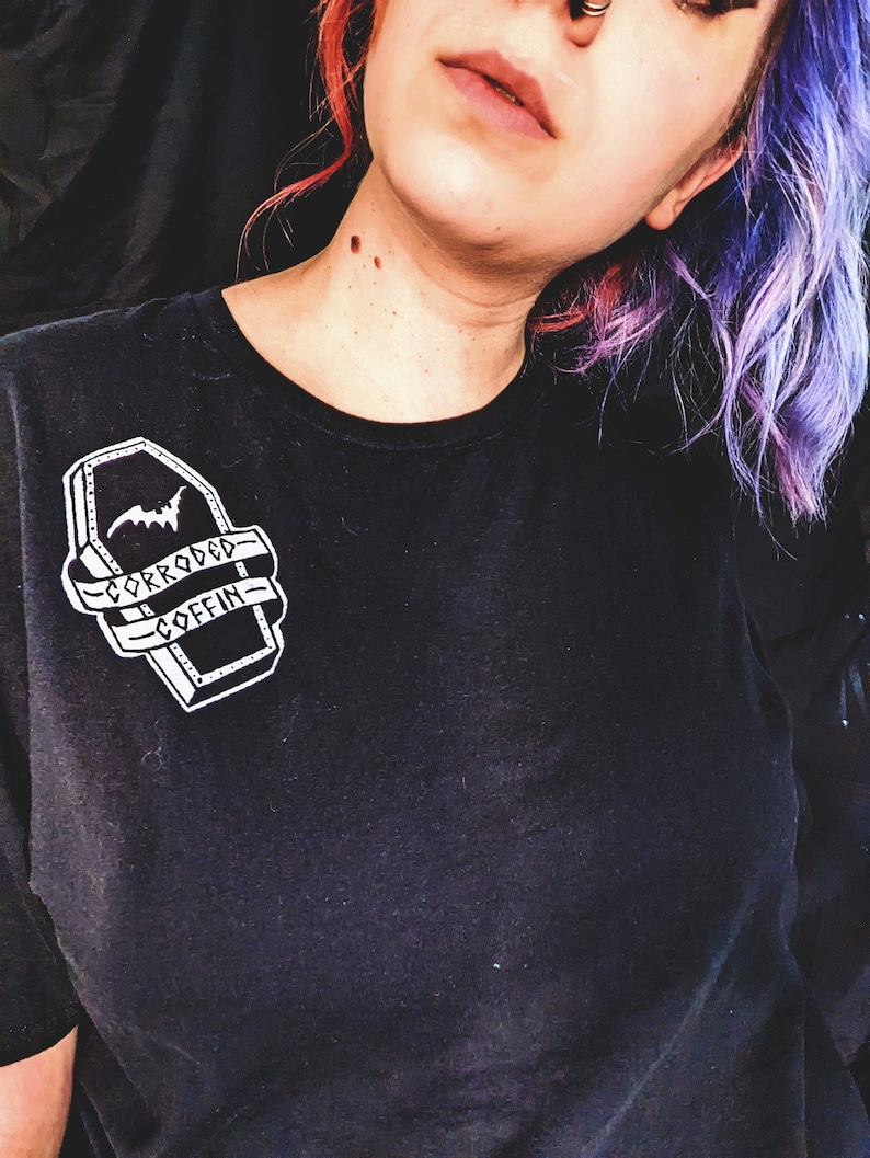 May include: Black t-shirt with a white graphic of a coffin with a bat and the text "Corroded Coffin".