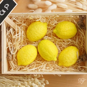 May include: A wooden crate filled with yellow lemon-shaped soaps, with a small chalkboard sign that reads "Soap" on top.