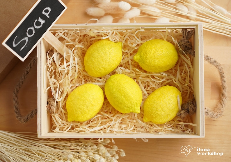 May include: A wooden crate filled with yellow lemon-shaped soaps, with a small chalkboard sign that reads "Soap" on top.